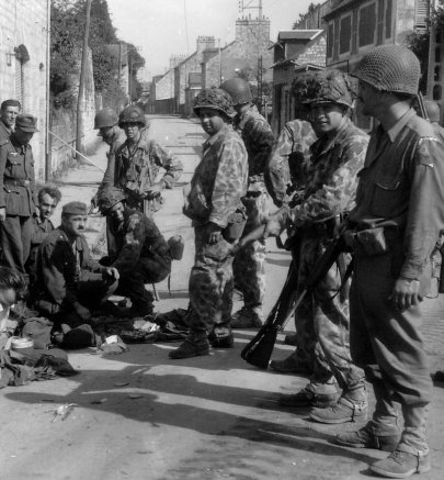 Soldats de la 2nd armored division avec des prisoniers dans une ville Normande.